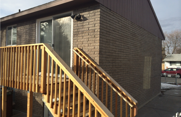 Repaired exterior of the same brick building featuring new siding and a freshly built wooden staircase and railing.