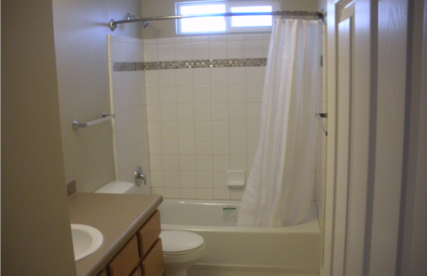 Fully restored bathroom with clean white tiles, a modern bathtub and shower, beige countertop with sink, and soft neutral-colored walls. The space appears bright and freshly renovated.