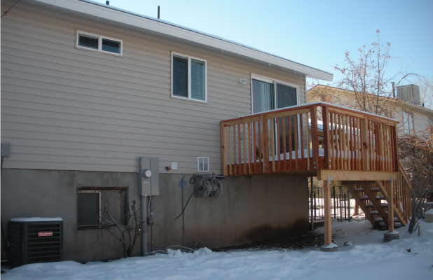 Restored exterior of a residential home after fire damage. The siding is fully repaired, windows replaced, and a new wooden deck with stairs has been installed. Snow covers the ground, and the area appears clean and maintained.